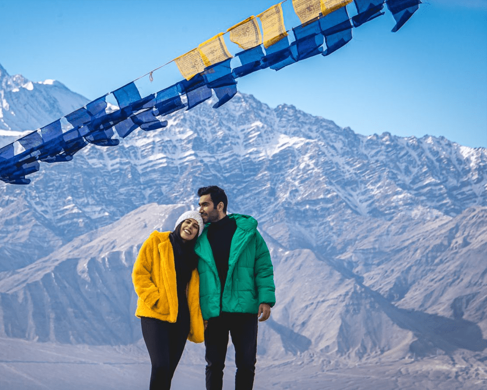 Couple under prayer flags with Himalayan peaks, Ladakh tour package